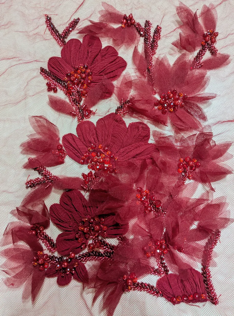 Deep red raised flowers, translucent petal shapes and glossy centres on a pale mesh ground.