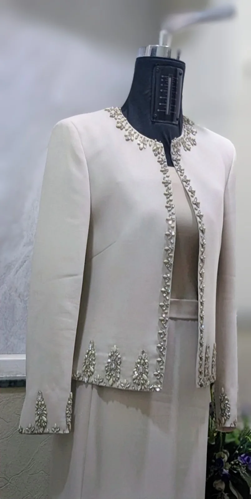 Pale jacket on a dress form, with reflective motifs along the neckline, front, hem and cuffs.