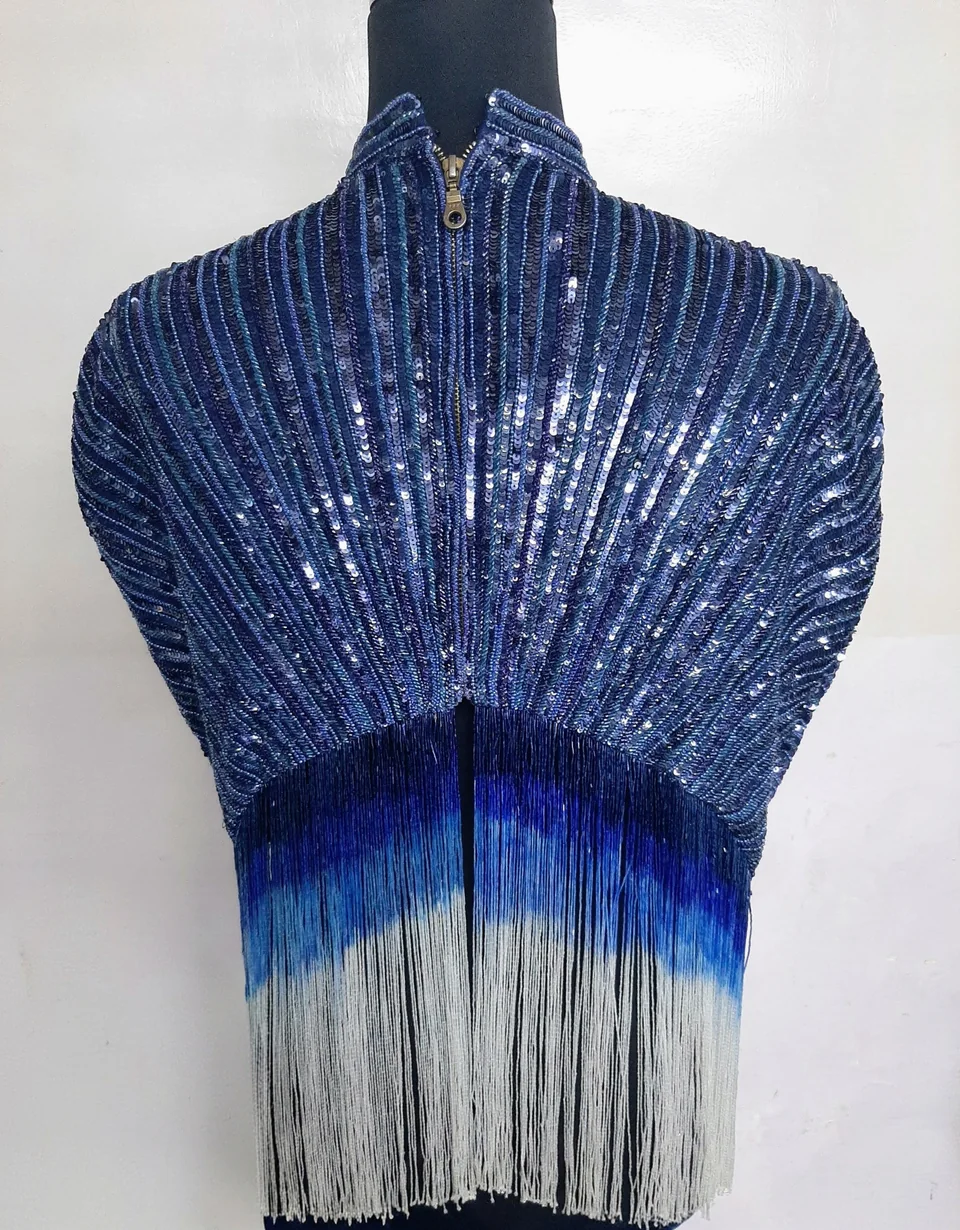 Deep blue embellished shoulder piece with radiating rows, a high collar and long blue-to-white fringe on a dress form.