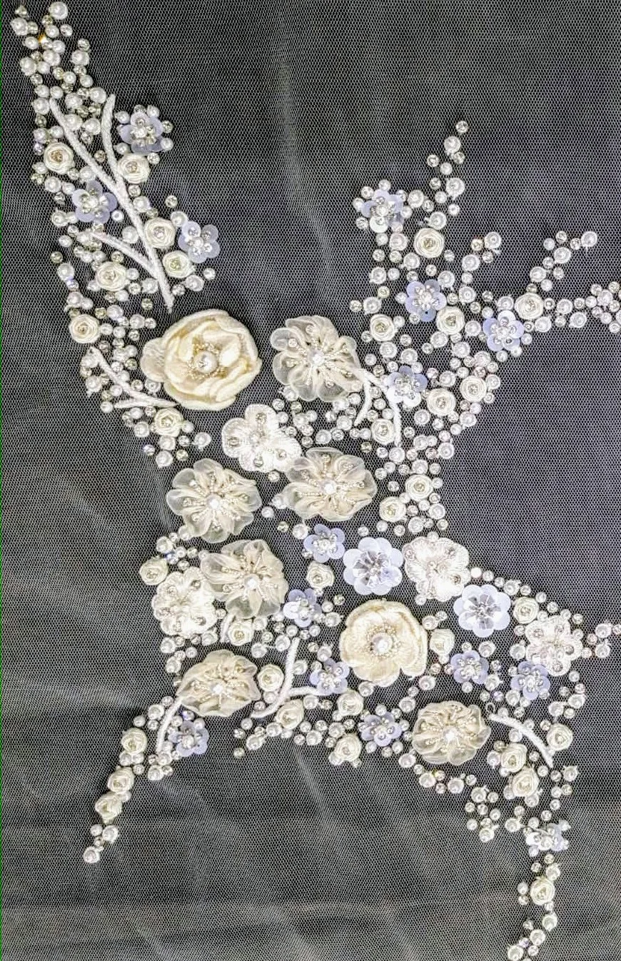 Branching arrangement of pale raised flowers and small rounded accents on transparent net.