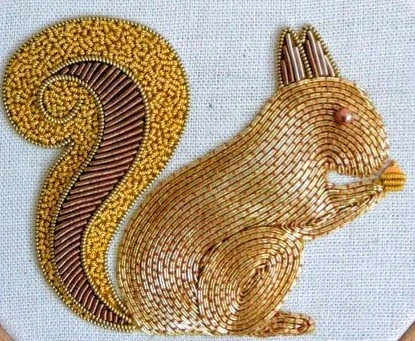 Gold-toned bead and metallic-thread embroidery forming a squirrel with a curled tail on pale fabric.