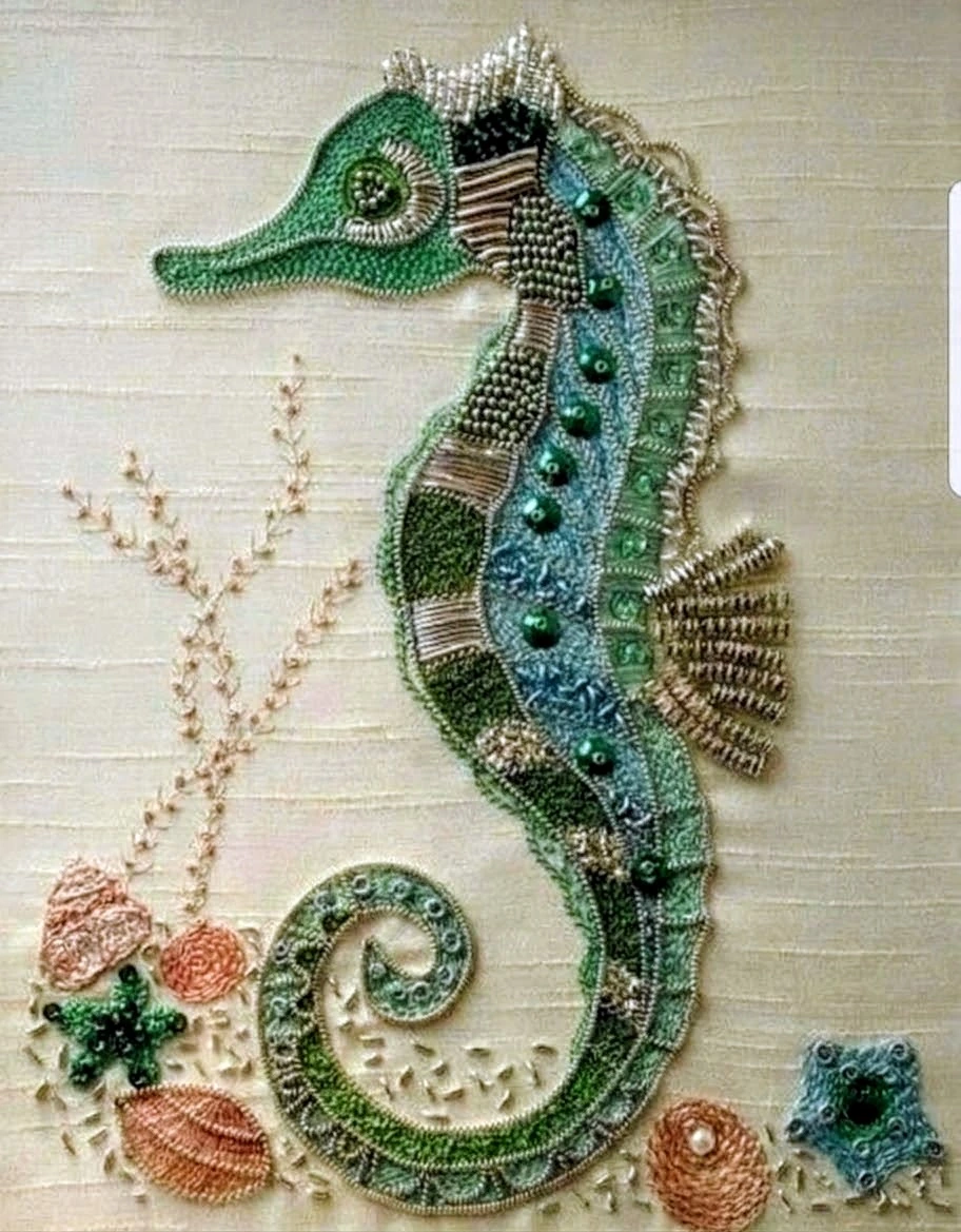 Green and gold-toned embroidered seahorse with a curled tail and small marine motifs on pale fabric.