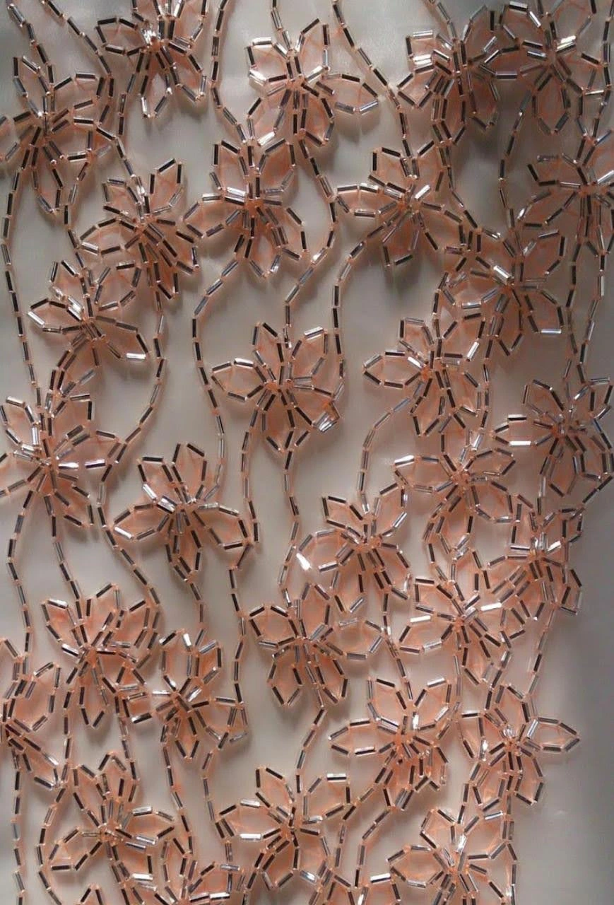 Repeating rose-gold-toned floral outlines made from elongated beads on sheer pale fabric.