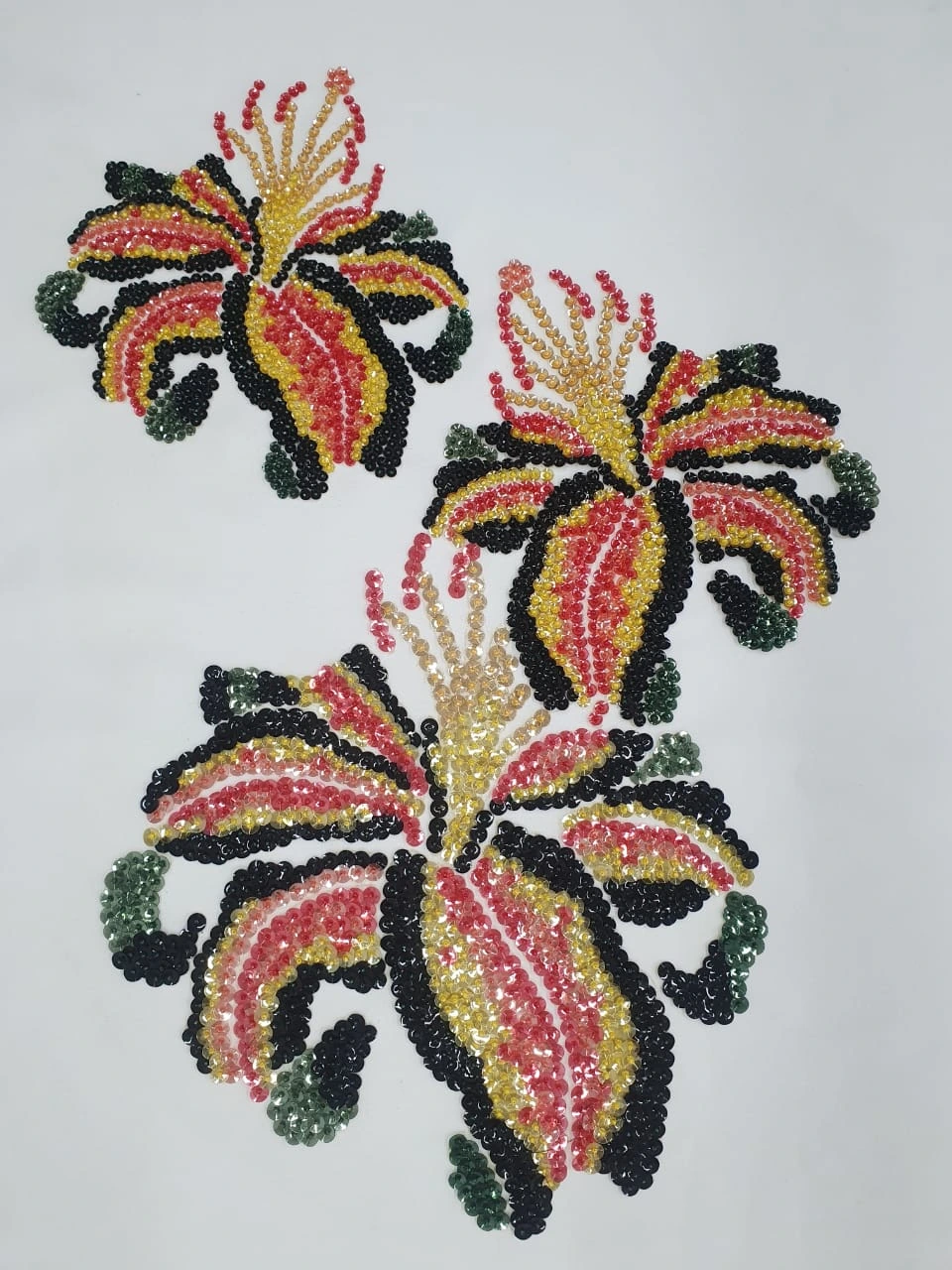 Three red and yellow embroidered flowers with dark green edges arranged diagonally on pale fabric.