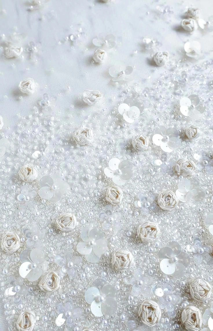 Small white ribbon roses, translucent beads and white sequins scattered over a pale textured embroidered surface.