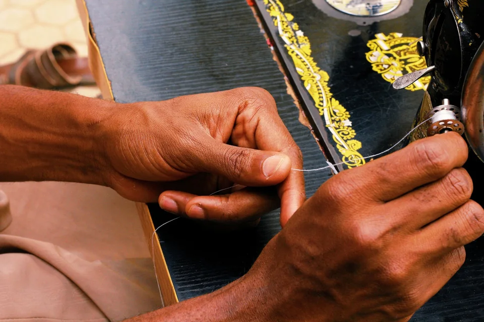 Close-up of hands guiding a thread at a traditional sewing machine.